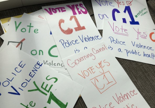 Signs on the ground reading "Vote YES on C1, Police Violence is a Public Health Issue"